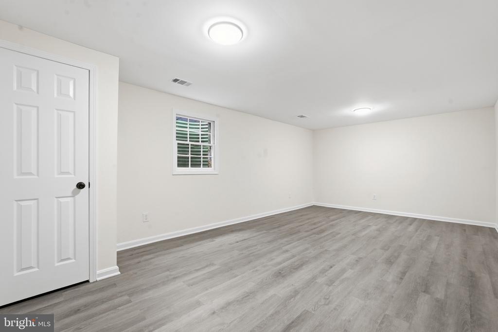 Empty room with gray wood-look flooring, white walls, a small window, and recessed lights.