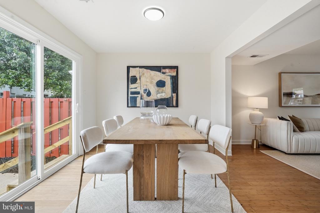 Dining room with a wooden table and white chairs beside sliding doors to a fenced deck.