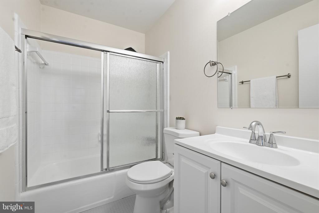 Bathroom with frosted sliding shower doors, a bathtub, toilet, and white vanity.