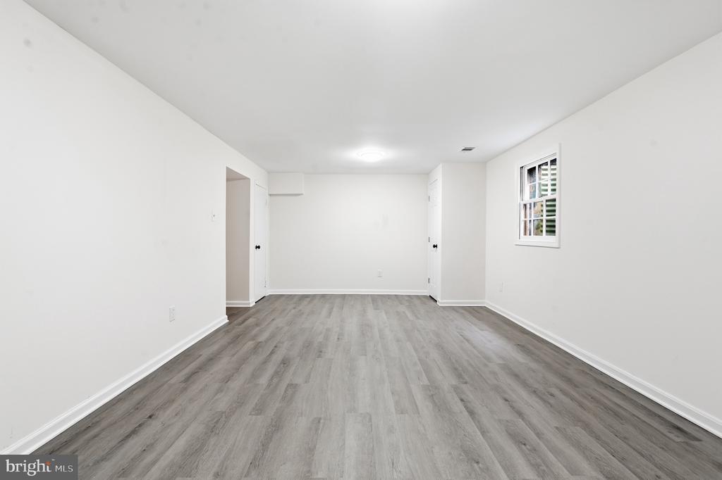Empty room with gray plank flooring, white walls, and a small window.