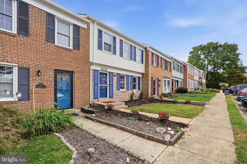 Attached townhouses with brick and light siding, blue shutters, landscaped front yards, and a sidewalk.