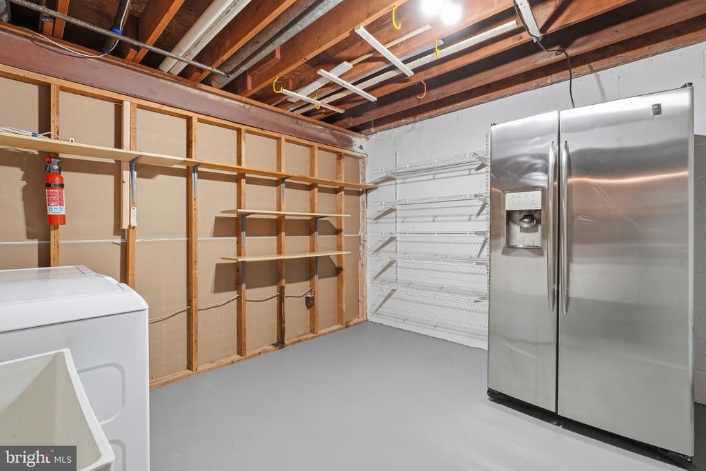 Basement laundry and storage room with a washer, stainless steel refrigerator, and open shelving.