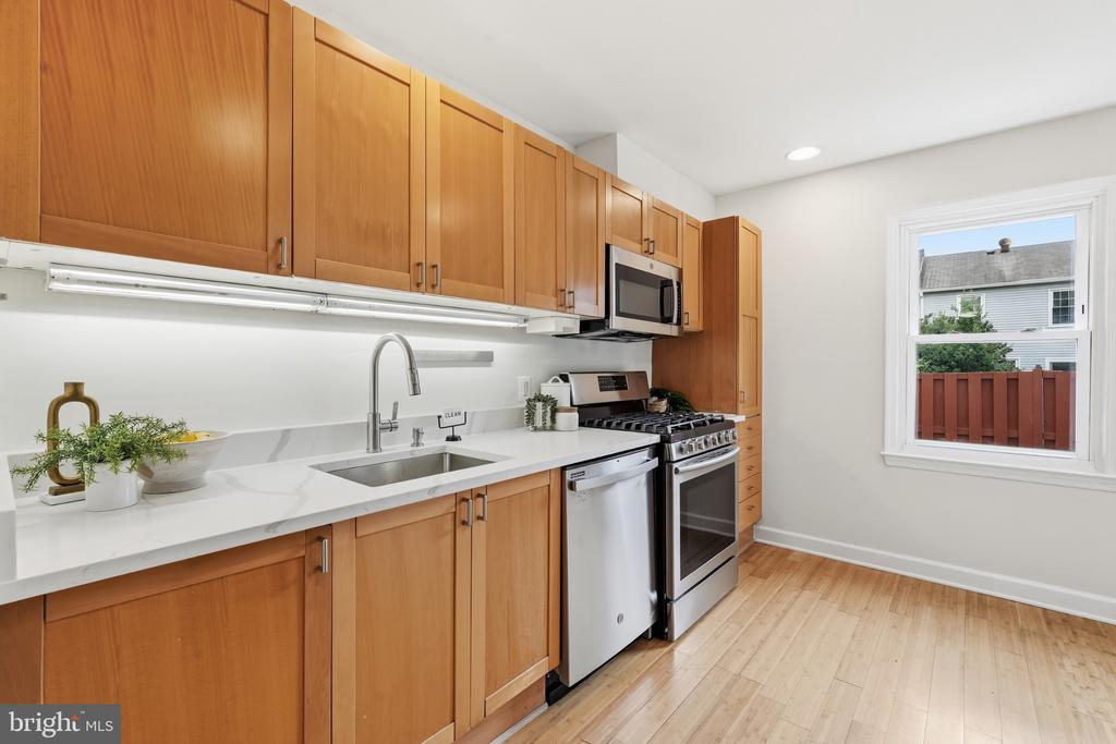 Kitchen with warm wood cabinets, white counters, stainless appliances, and a window overlooking a fenced yard.