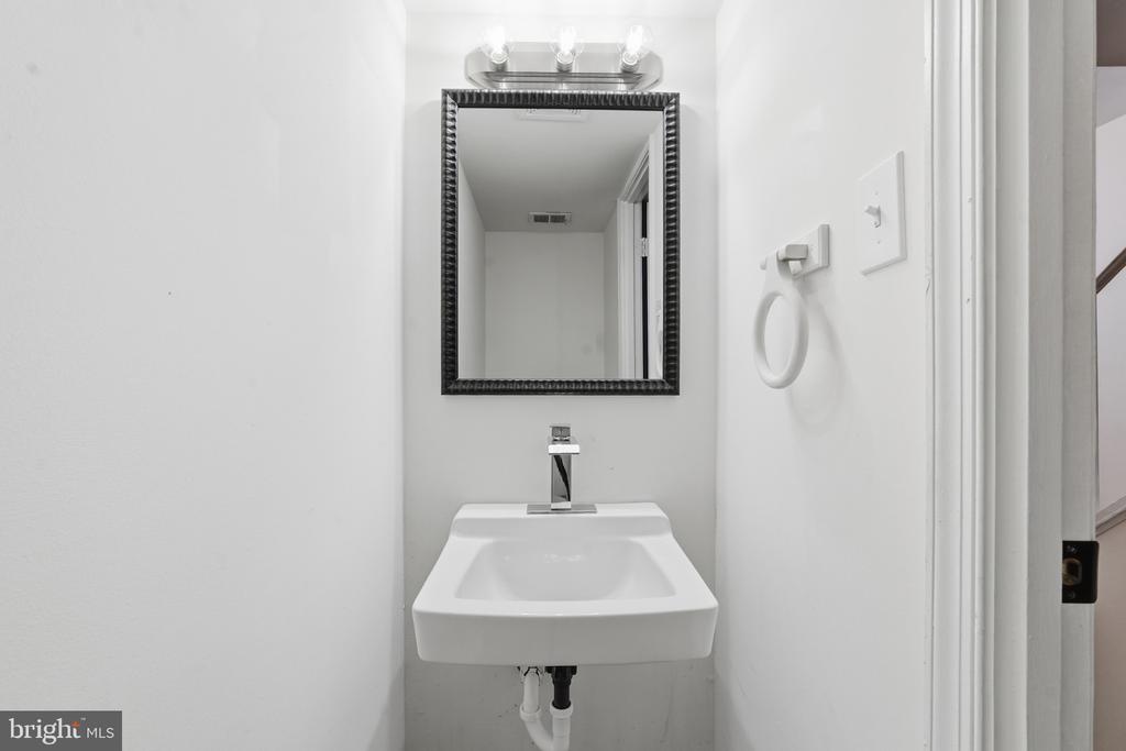Compact bathroom with a wall-mounted sink, dark-framed mirror, and towel ring.