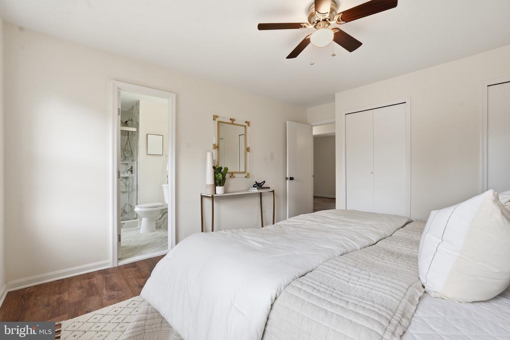 Bedroom with white bedding, a ceiling fan, and a doorway to an ensuite bathroom.