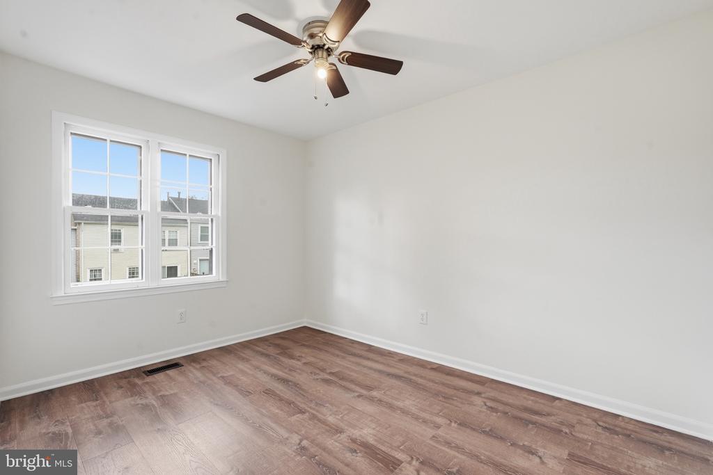 Empty bedroom with wood-look flooring, two windows, and a ceiling fan.