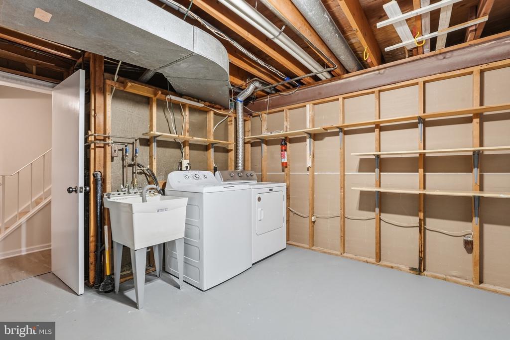Basement laundry area with washer, dryer, utility sink, and open shelving.
