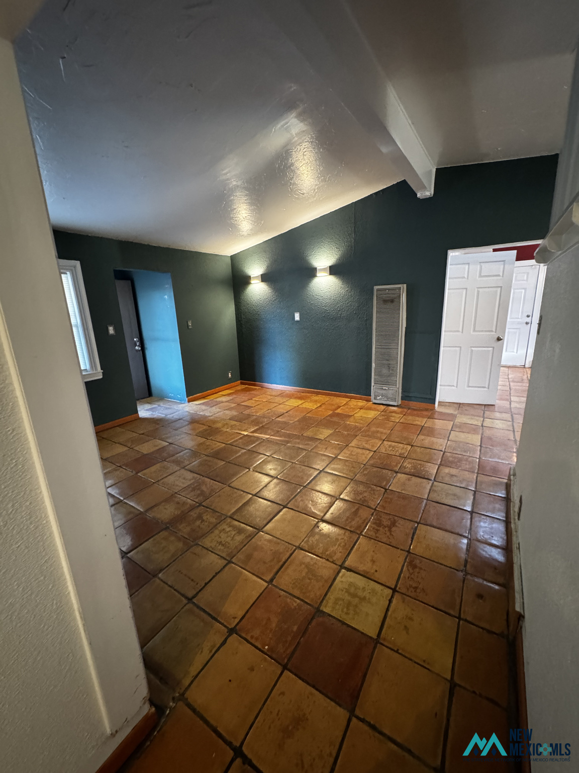 Vacant room with dark green walls, terracotta tile flooring, and a high angled ceiling.