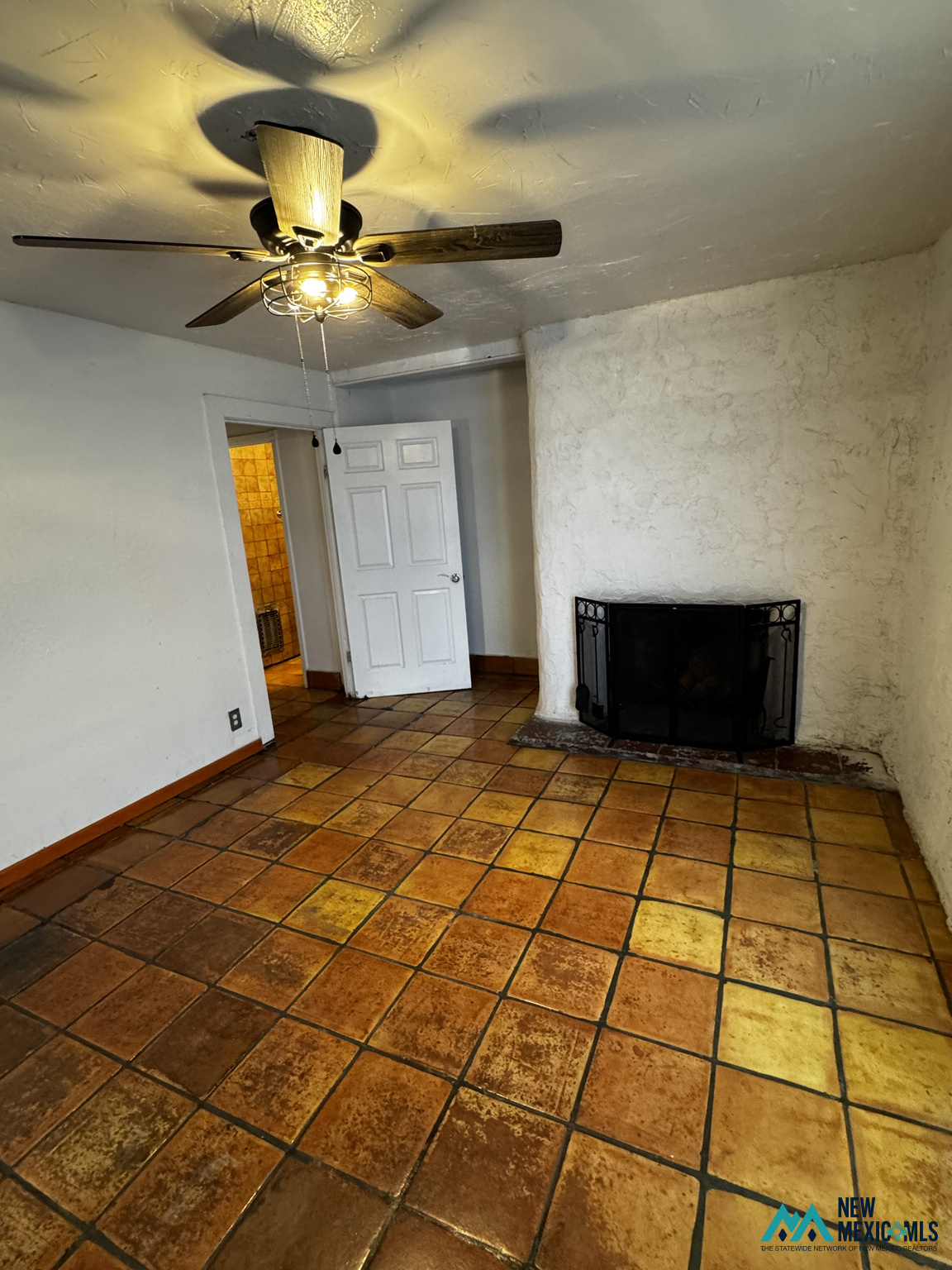 Unfurnished room with terracotta tile floors, a white fireplace wall, and a lit ceiling fan.