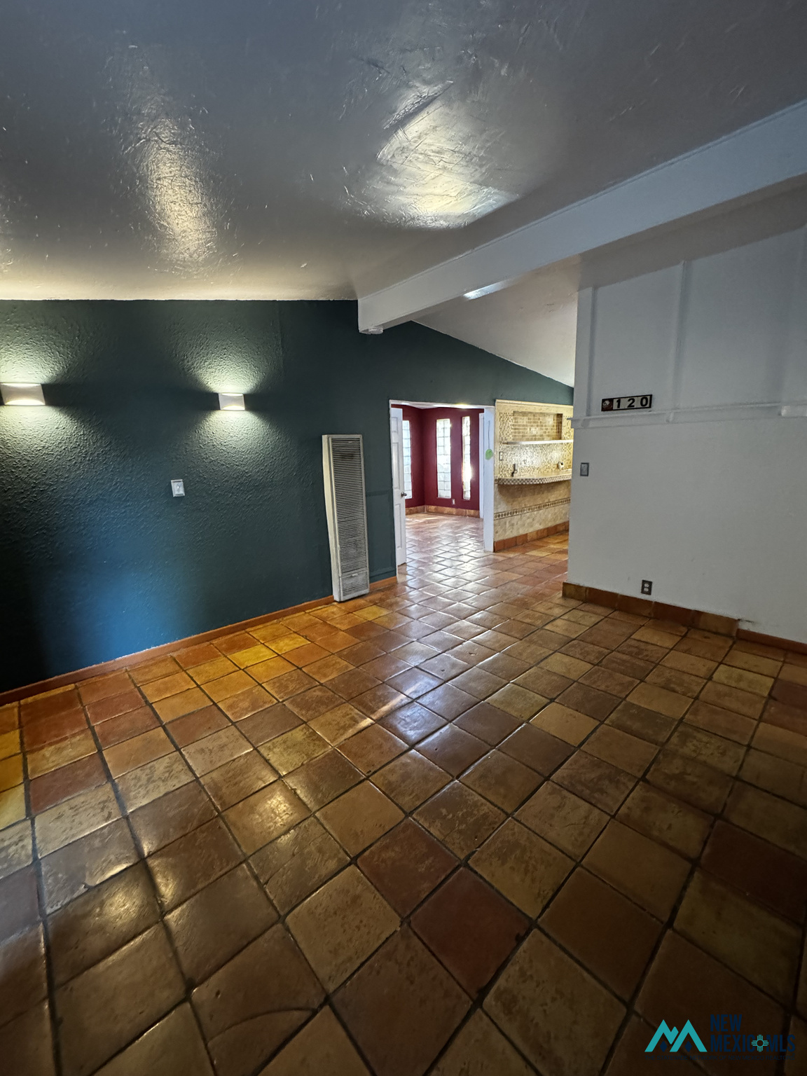 Vacant room with terracotta tile floors and a dark teal wall, opening to a tiled kitchen.