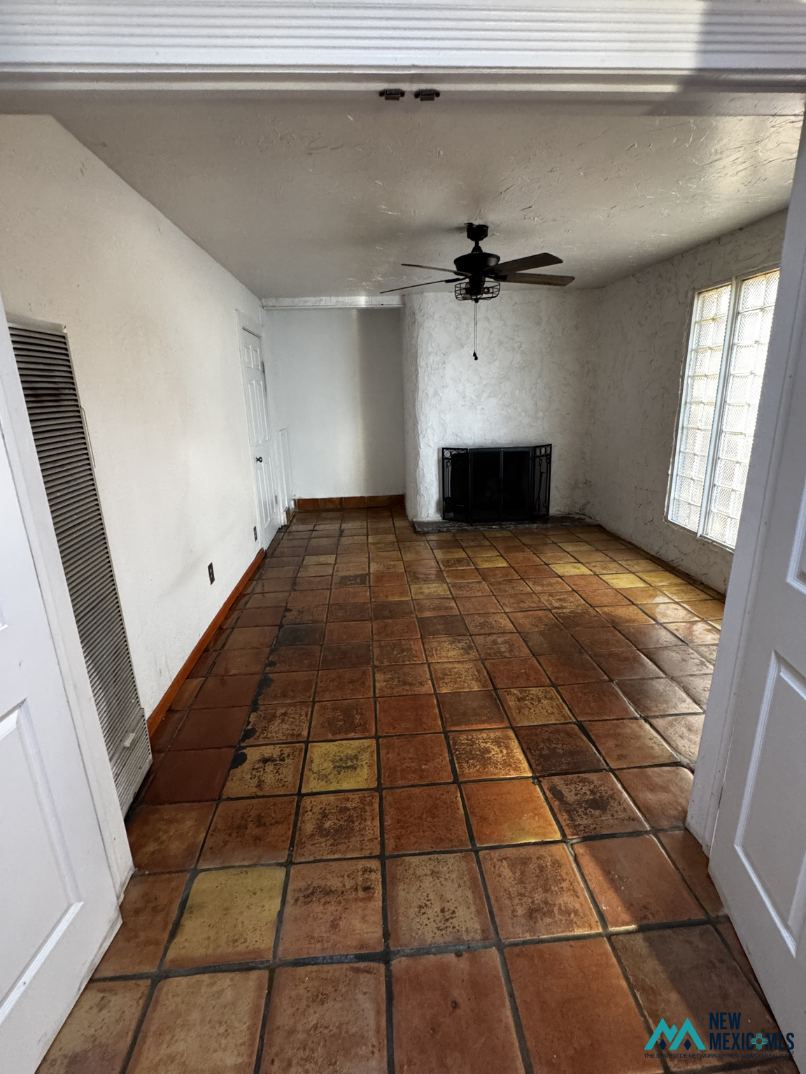 Empty living room with terracotta tile floors, a black fireplace, and glass-block windows.