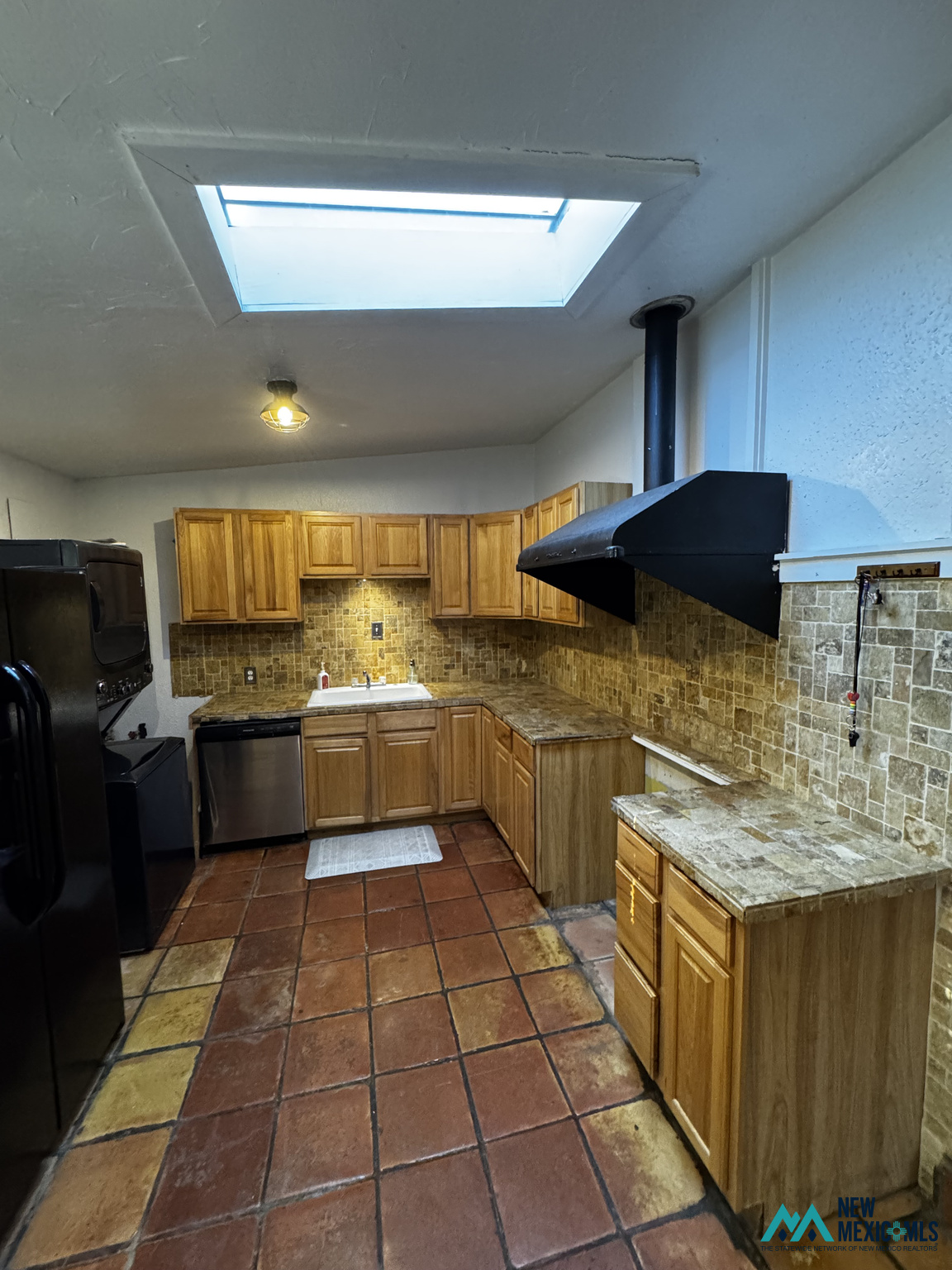 Kitchen with wood cabinets, tiled backsplash and floors, black appliances, and a large skylight.