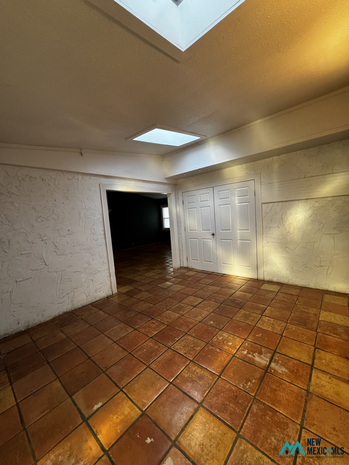 Empty room with terracotta tile floors, textured walls, white closet doors, and skylights.