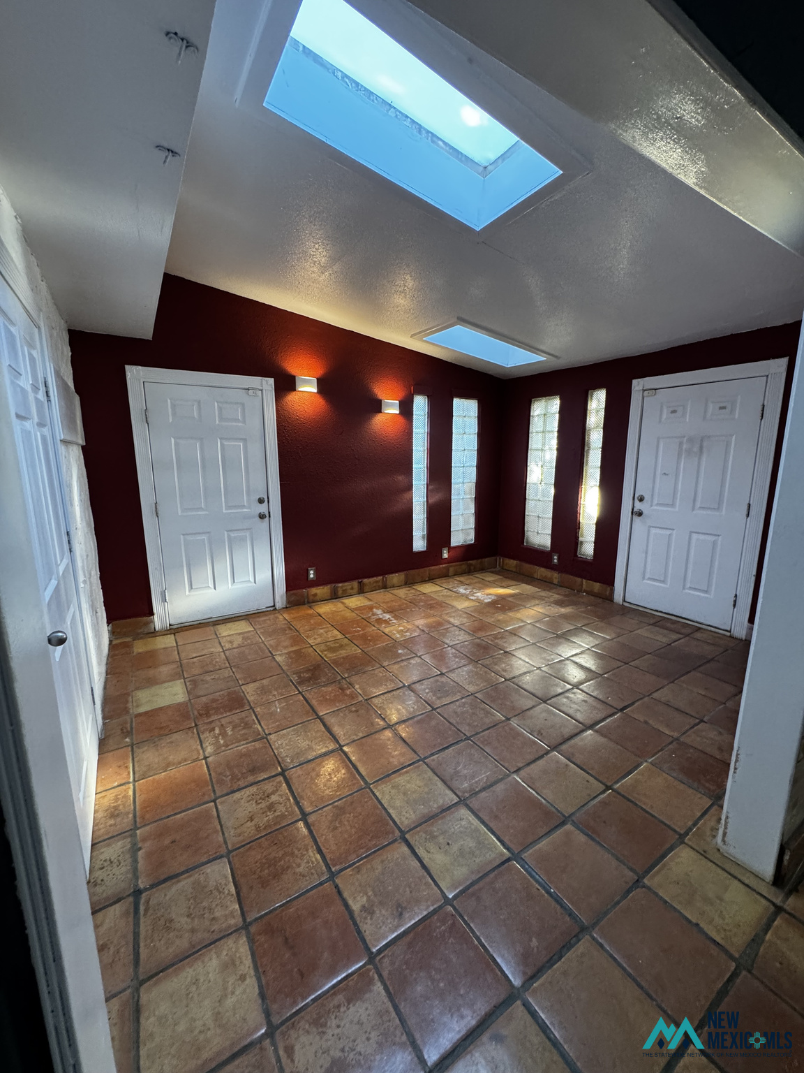 Empty room with terracotta tile, burgundy walls, glass-block windows, and skylights.
