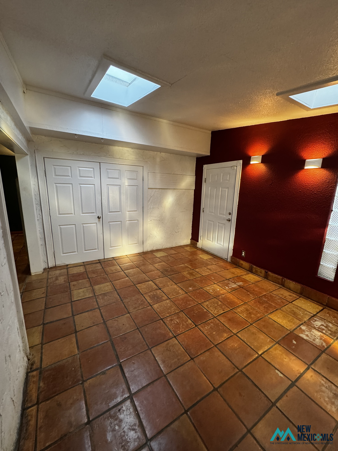 Empty entry area with terracotta tile floors, skylights, white doors, and a deep red accent wall.