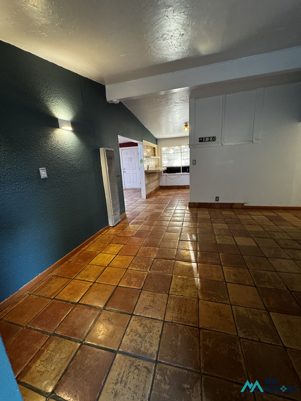 Empty tiled room with a dark teal wall and an opening to a counter and window.
