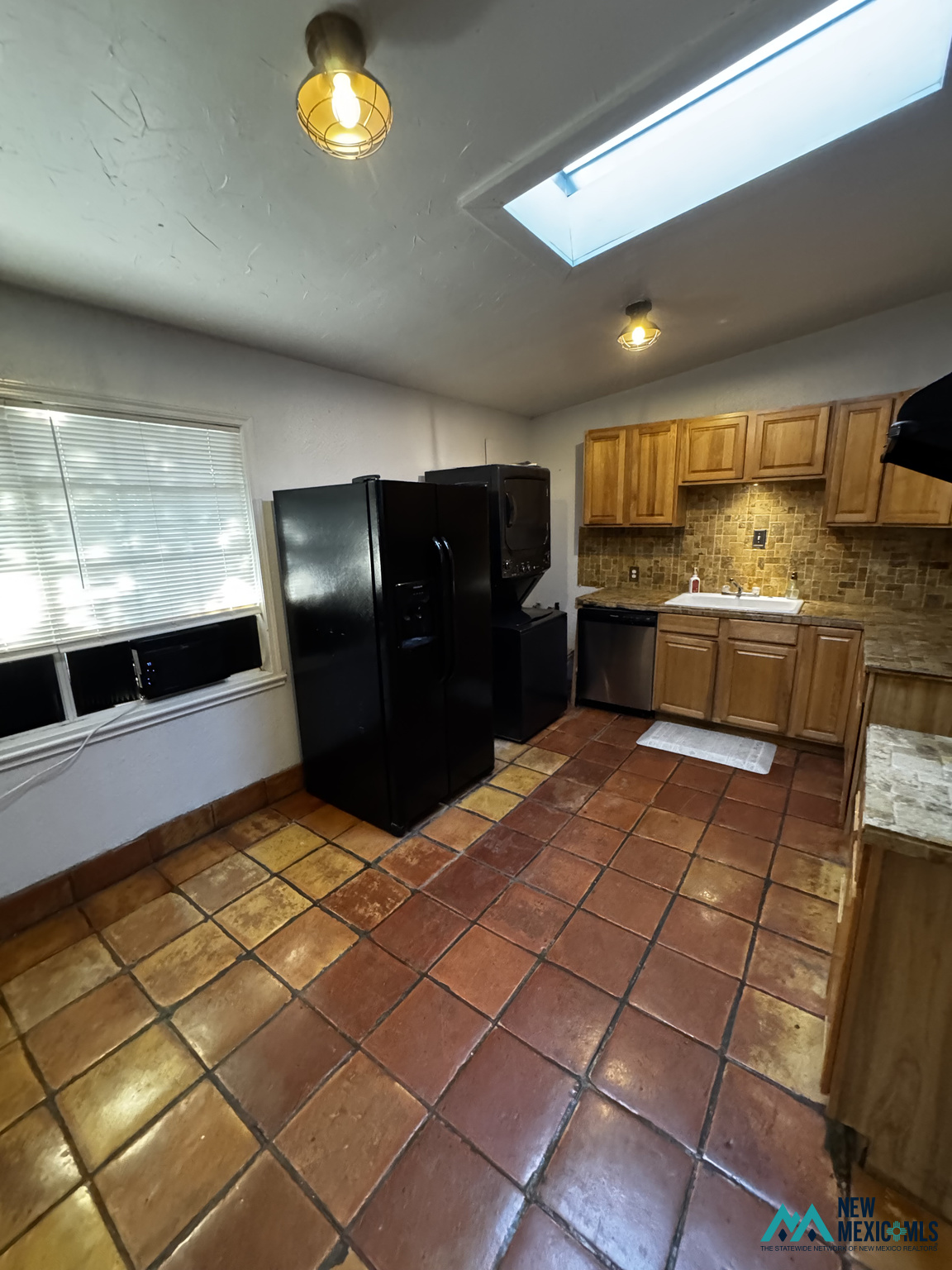 Kitchen with wood cabinets, stone-tile backsplash, black appliances, and colorful square tile flooring.