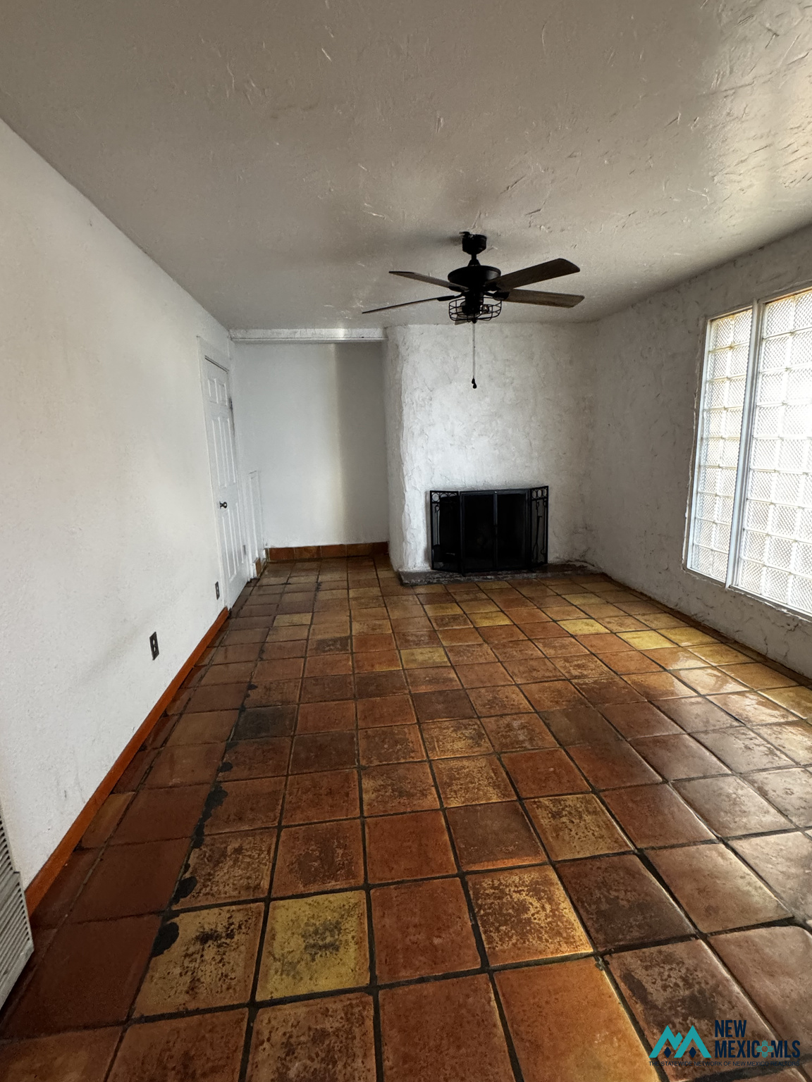 Vacant living room with terracotta tile floors, a black fireplace, ceiling fan, and tall gridded windows.