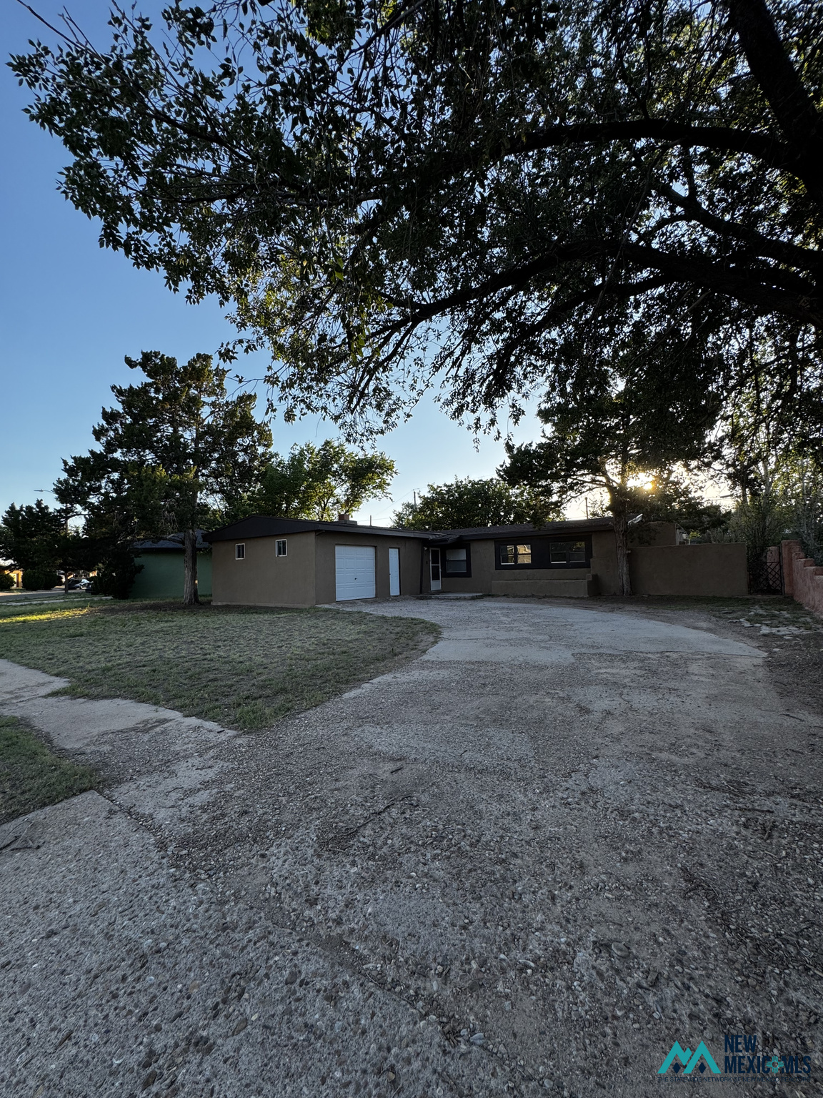 Single-story stucco home with a white garage door, broad driveway, and mature trees.