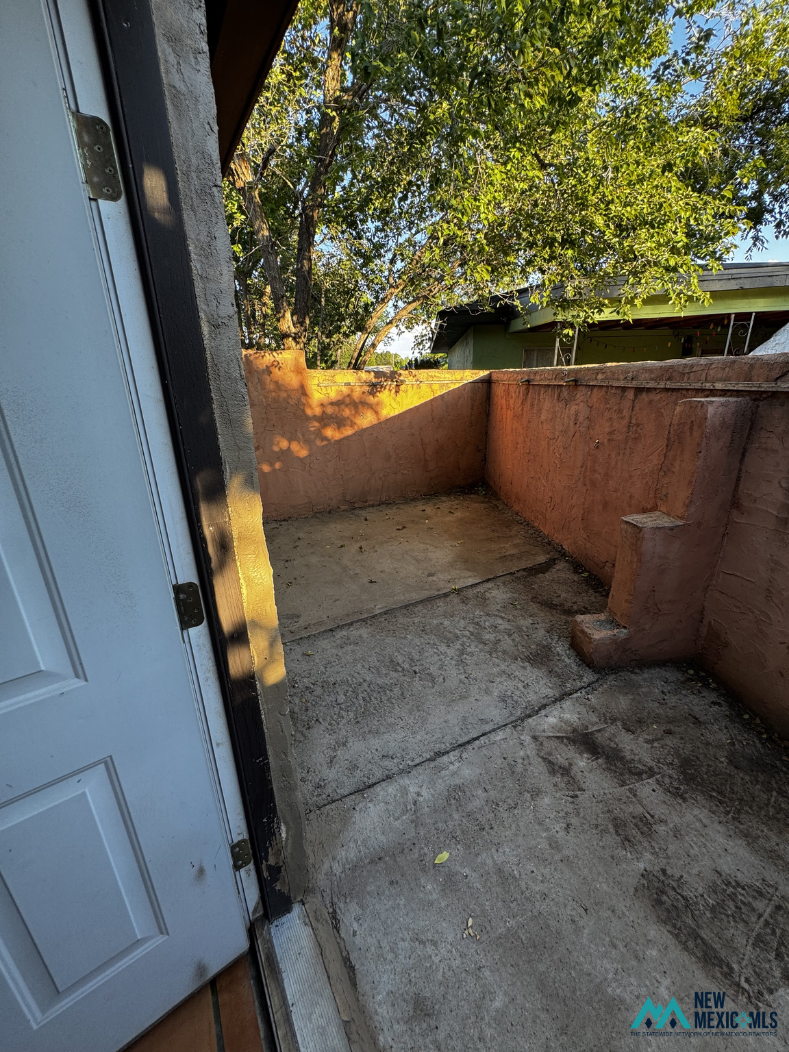 Concrete patio enclosed by terracotta stucco walls beneath leafy trees.