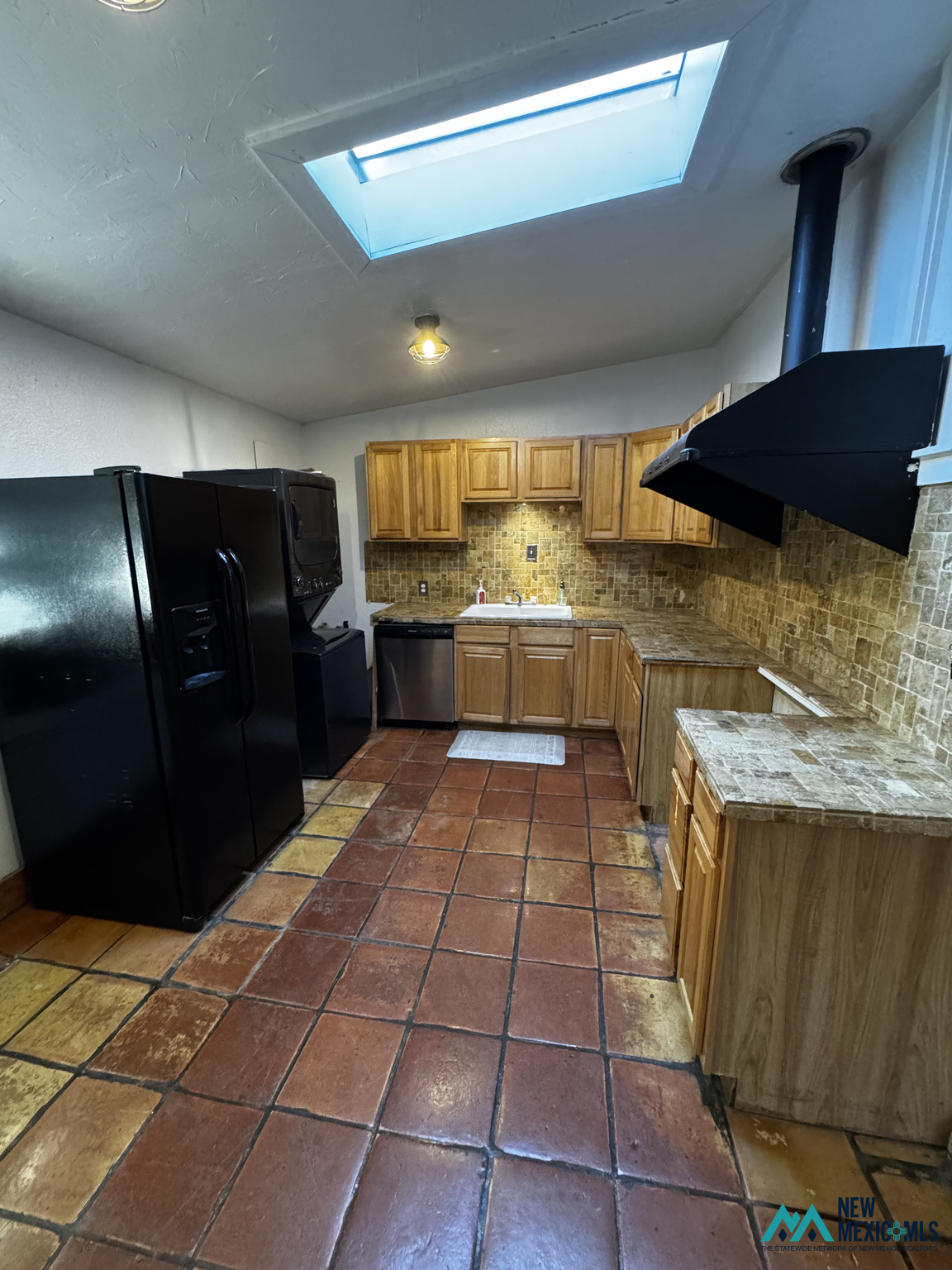 Kitchen with wood cabinets, terracotta tile flooring, black appliances, and a large skylight.