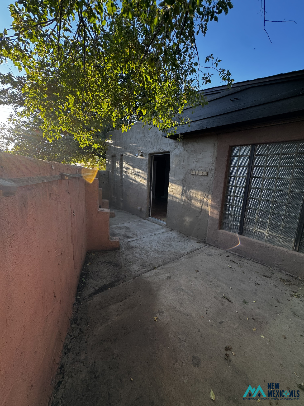 Concrete patio beside a stucco building, shaded by a leafy tree and bordered by a pink wall.