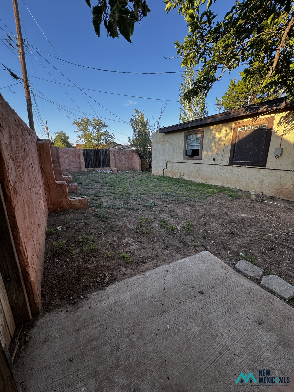 Backyard with reddish stucco walls, sparse ground cover, and a concrete patio beside the house.