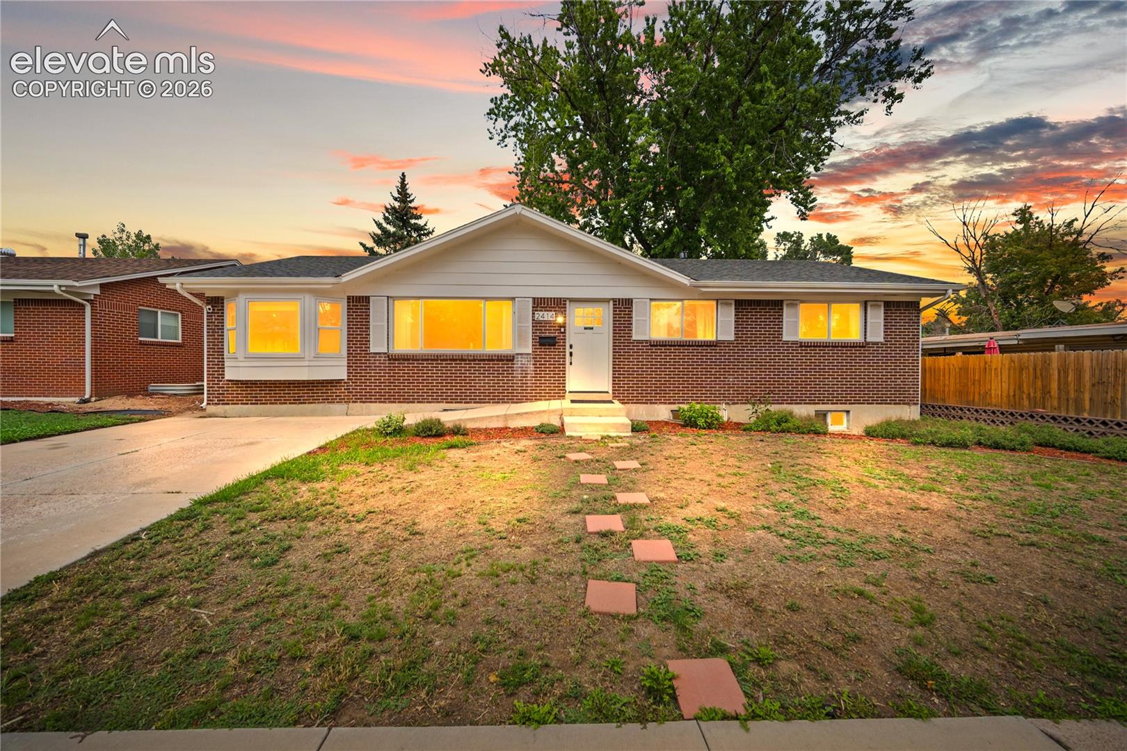 Brick ranch home with warmly lit windows, a bay window, and stepping stones at sunset.
