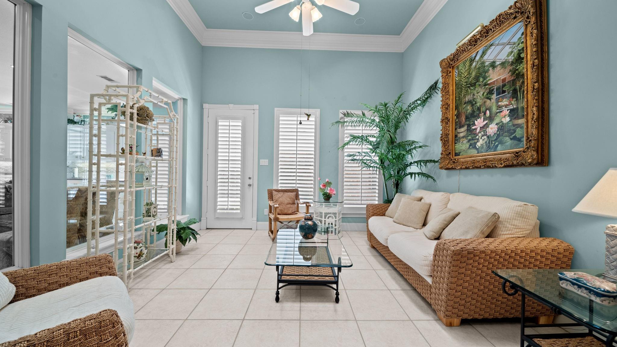 Living room with aqua walls, wicker seating, tiled floors, and an ornate floral painting.