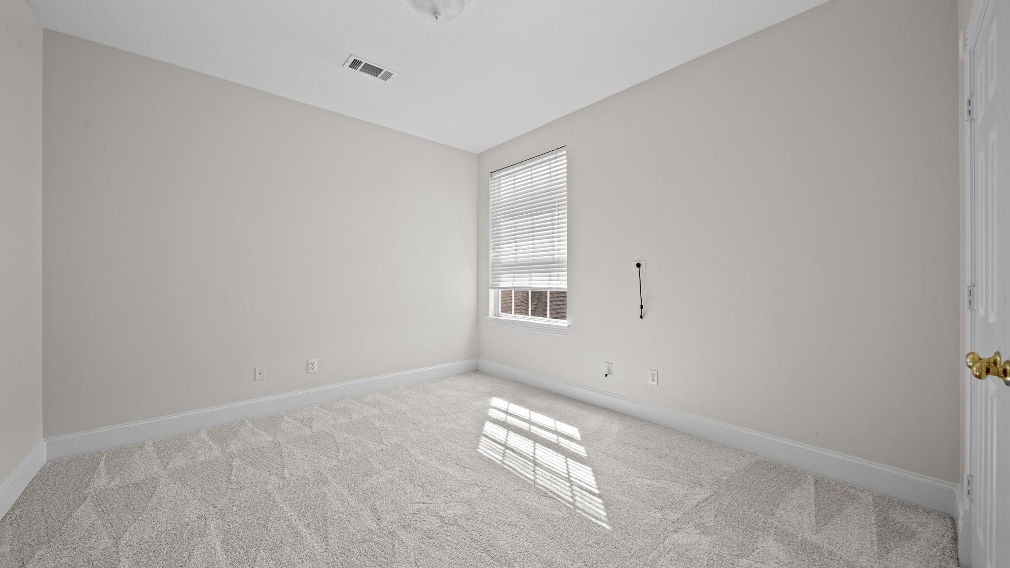 Empty carpeted bedroom with a window and blinds casting sunlight across the floor.