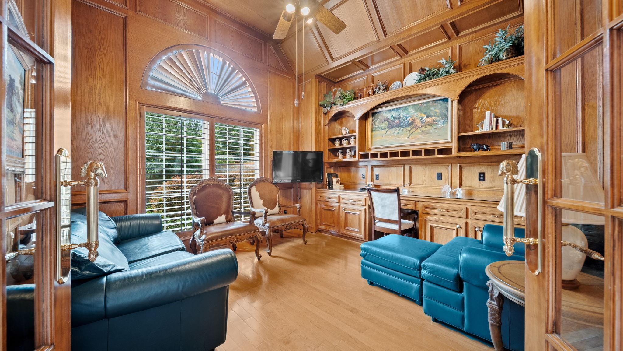 Wood-paneled living room with built-in shelves, shuttered windows, and blue leather sofas.