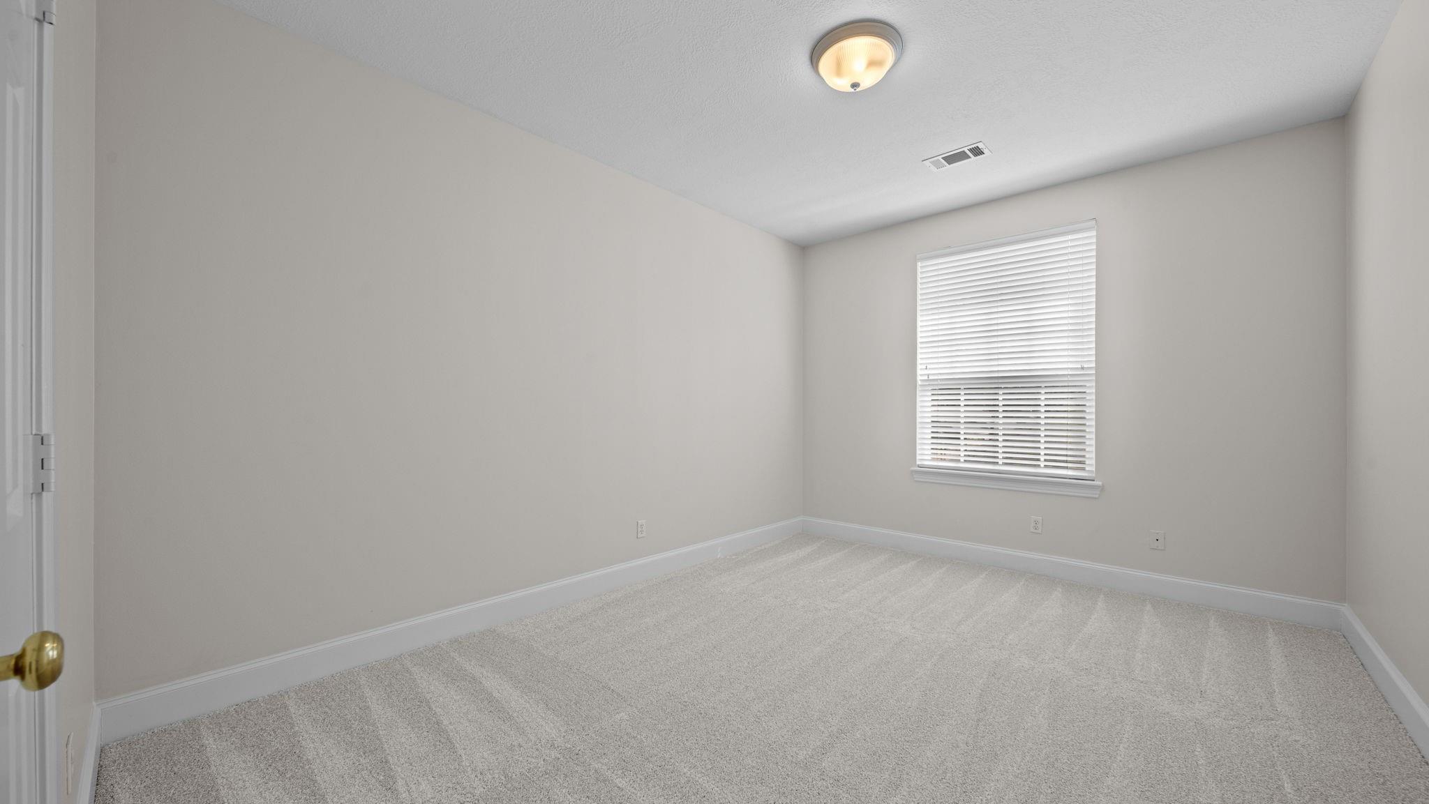 Empty bedroom with light carpet and a window fitted with white blinds.