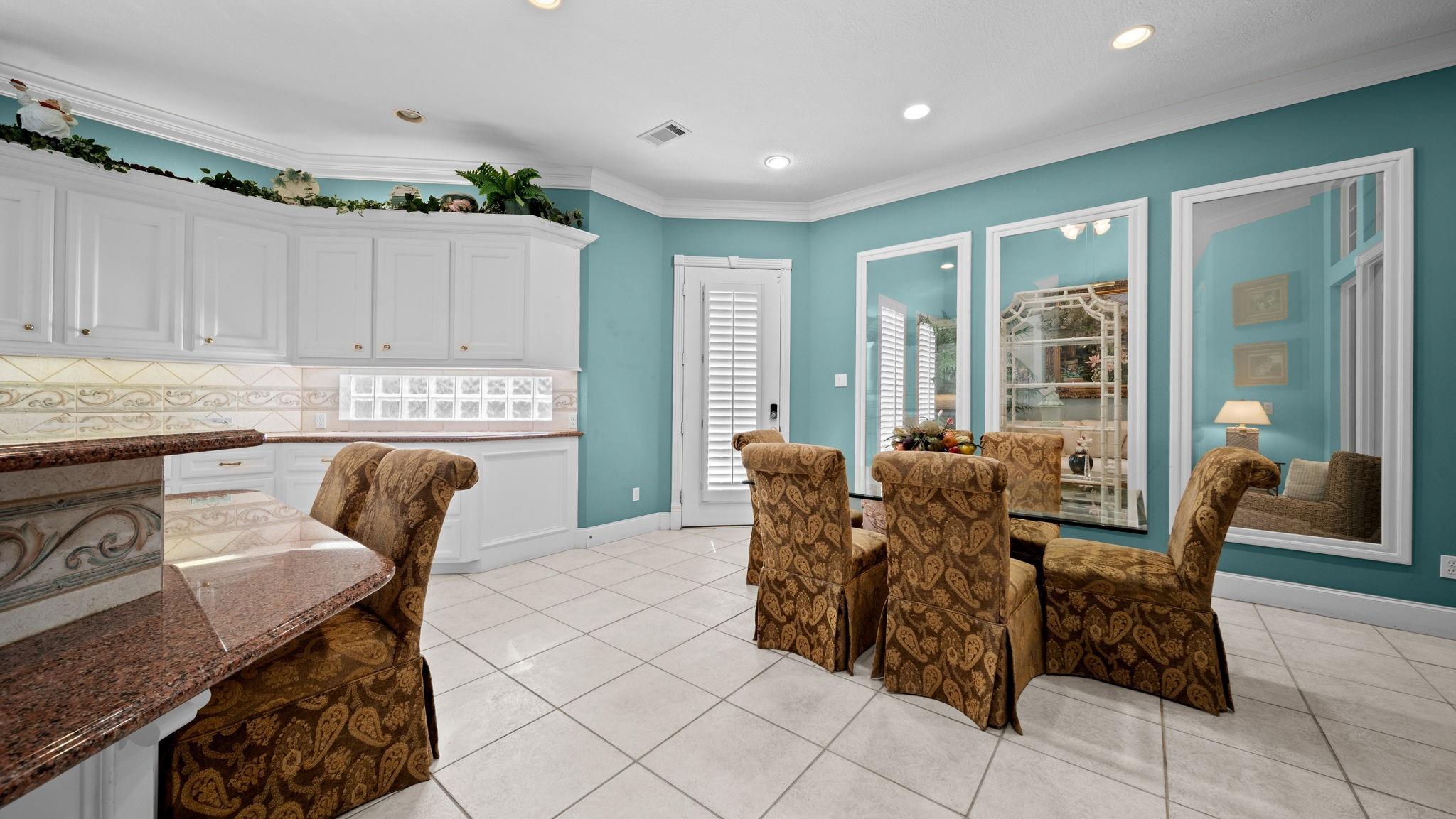 Dining area with turquoise walls, white cabinets, and brown patterned chairs around a glass-top table.