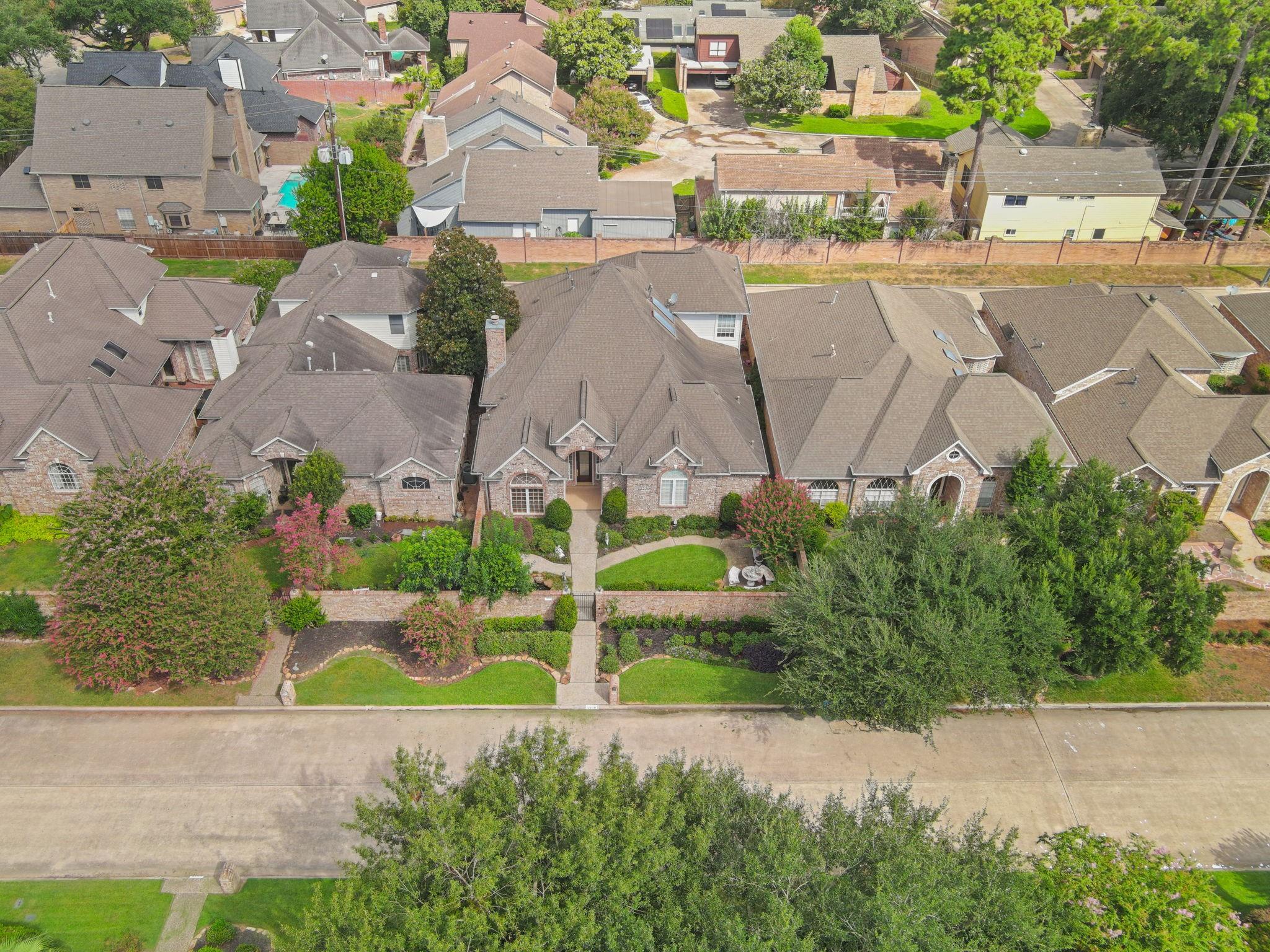 Aerial view of a brick home with a landscaped yard, curved walkway, and flowering trees.