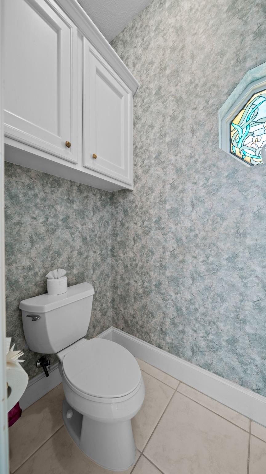 Bathroom with gray-green textured walls, white toilet and cabinets, and a stained-glass window.