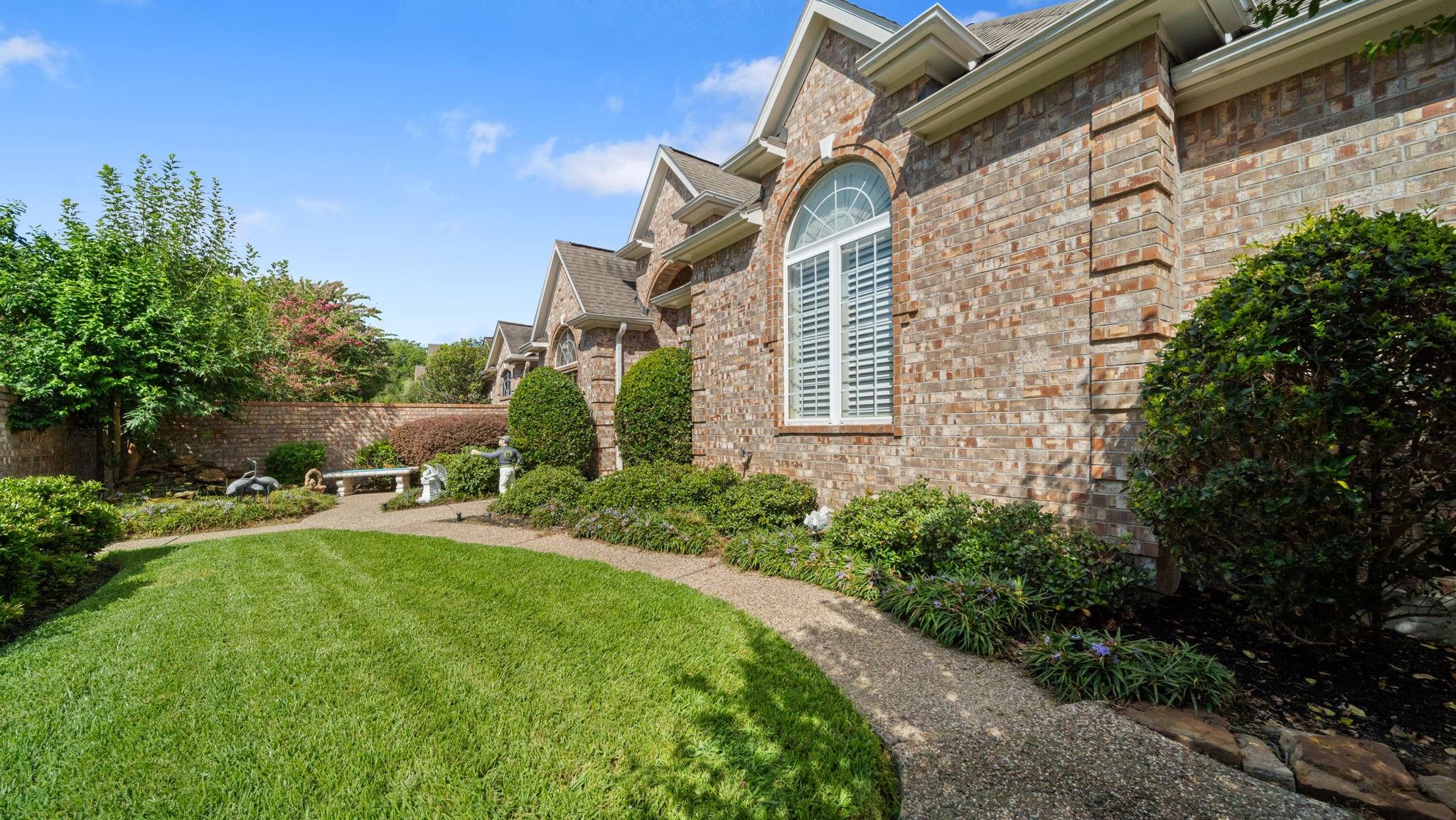 Brick home with arched windows beside a curved garden walkway and manicured lawn.