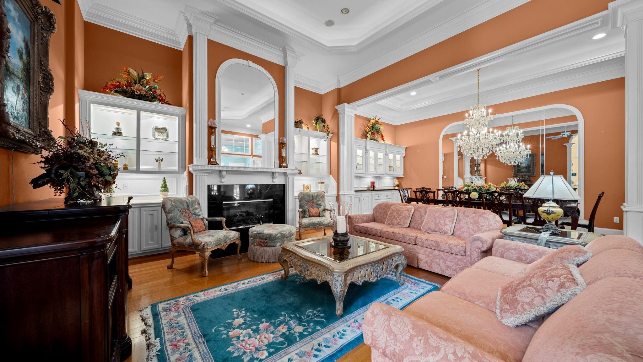 Living room with a fireplace, pink sofas, ornate white trim, and a blue floral rug.