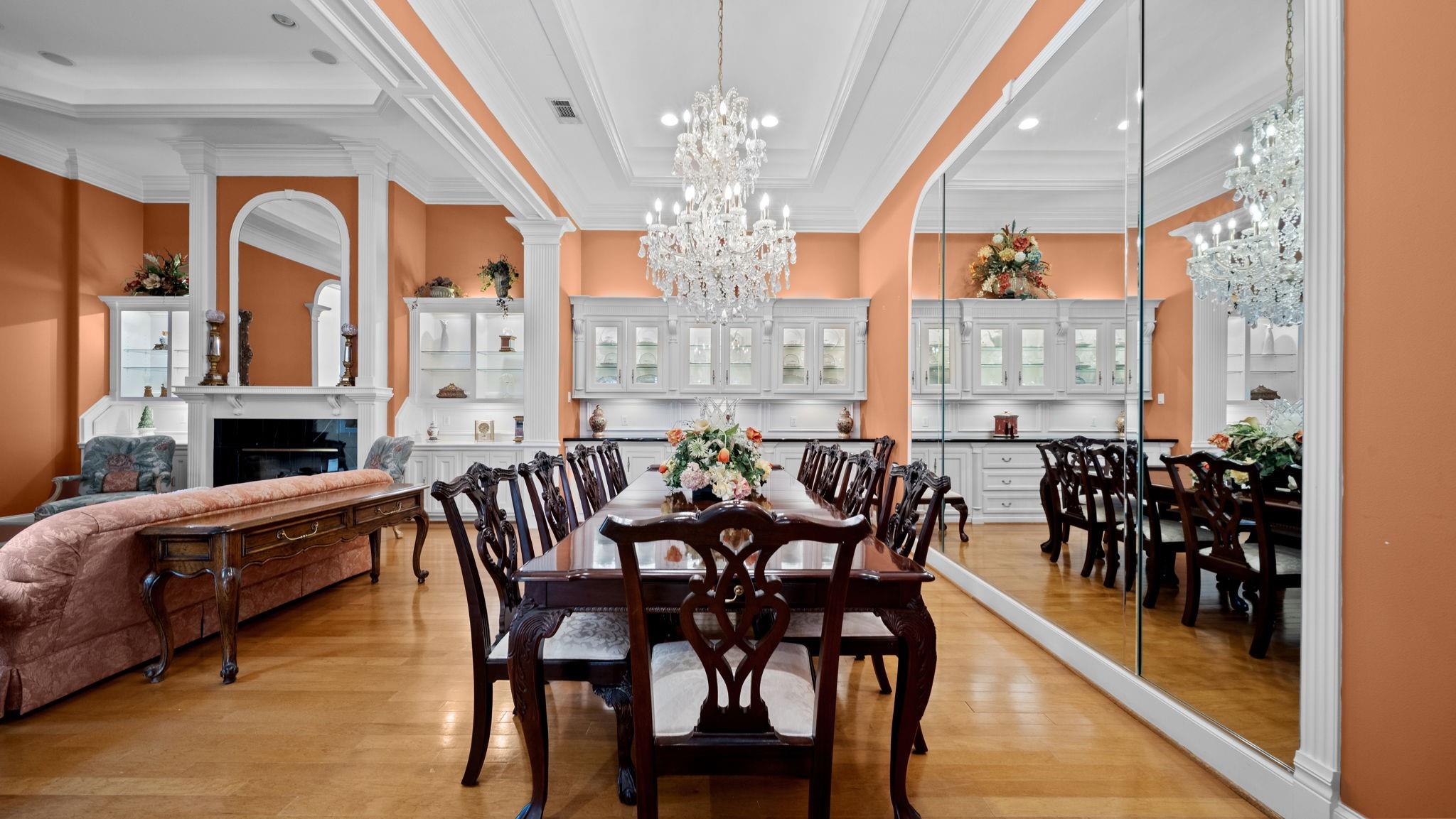 Formal dining room with a crystal chandelier, long carved-wood table, mirrored wall, and fireplace.