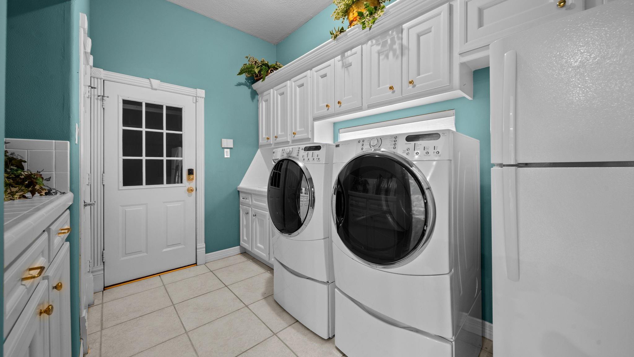 Laundry room with front-loading washer and dryer beneath white cabinets against turquoise walls.
