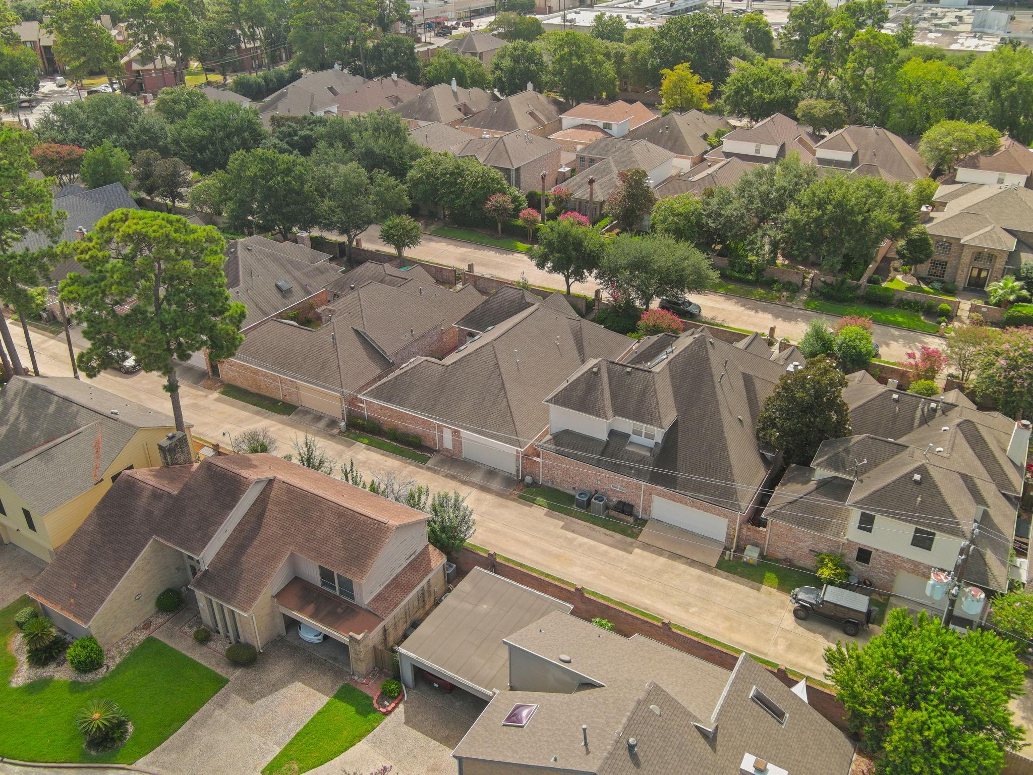 Aerial view of a residential street with brick homes, mature trees, and green lawns.