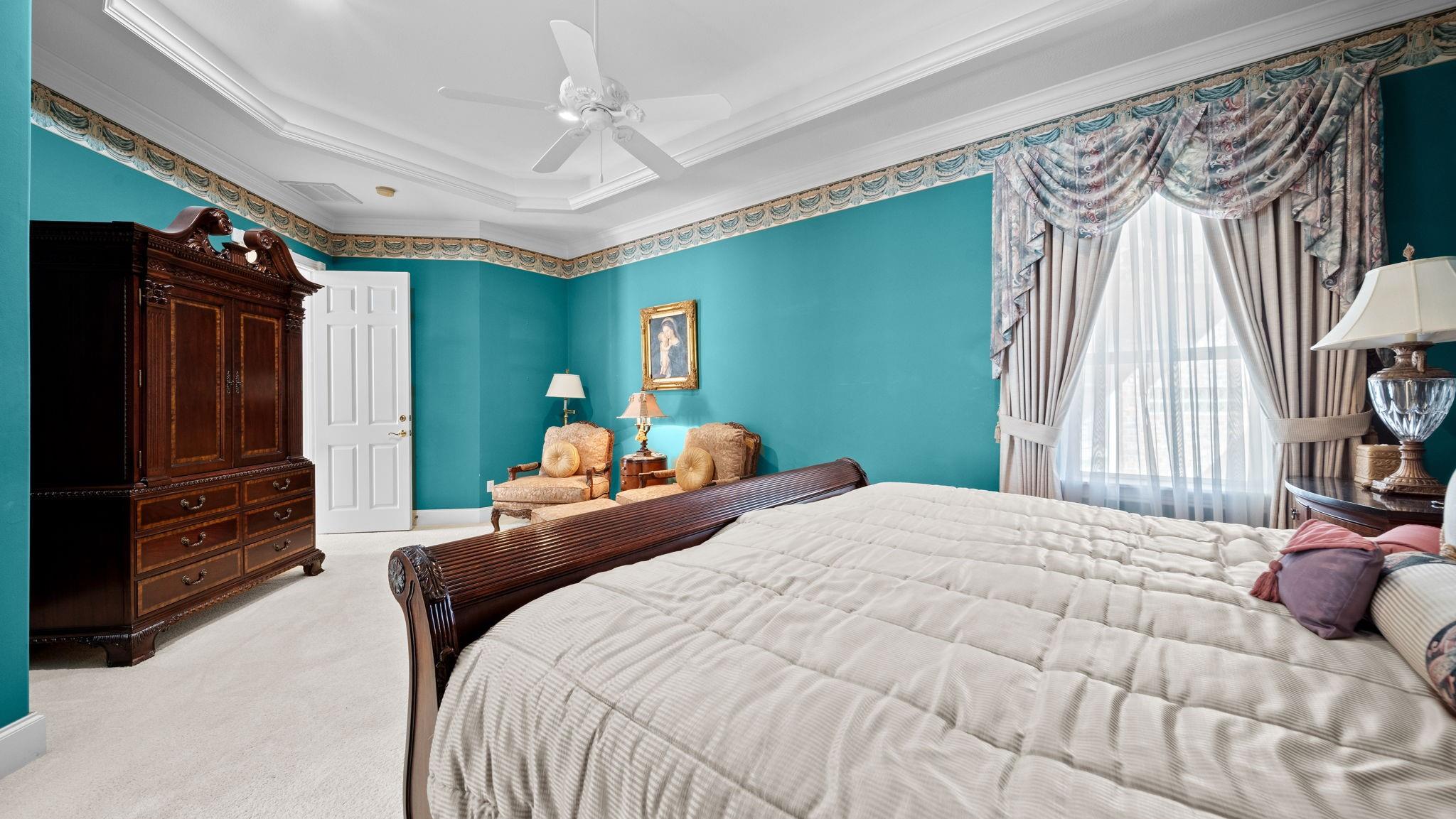 Bedroom with turquoise walls, carved wooden bed, matching armoire, and ornate curtains.