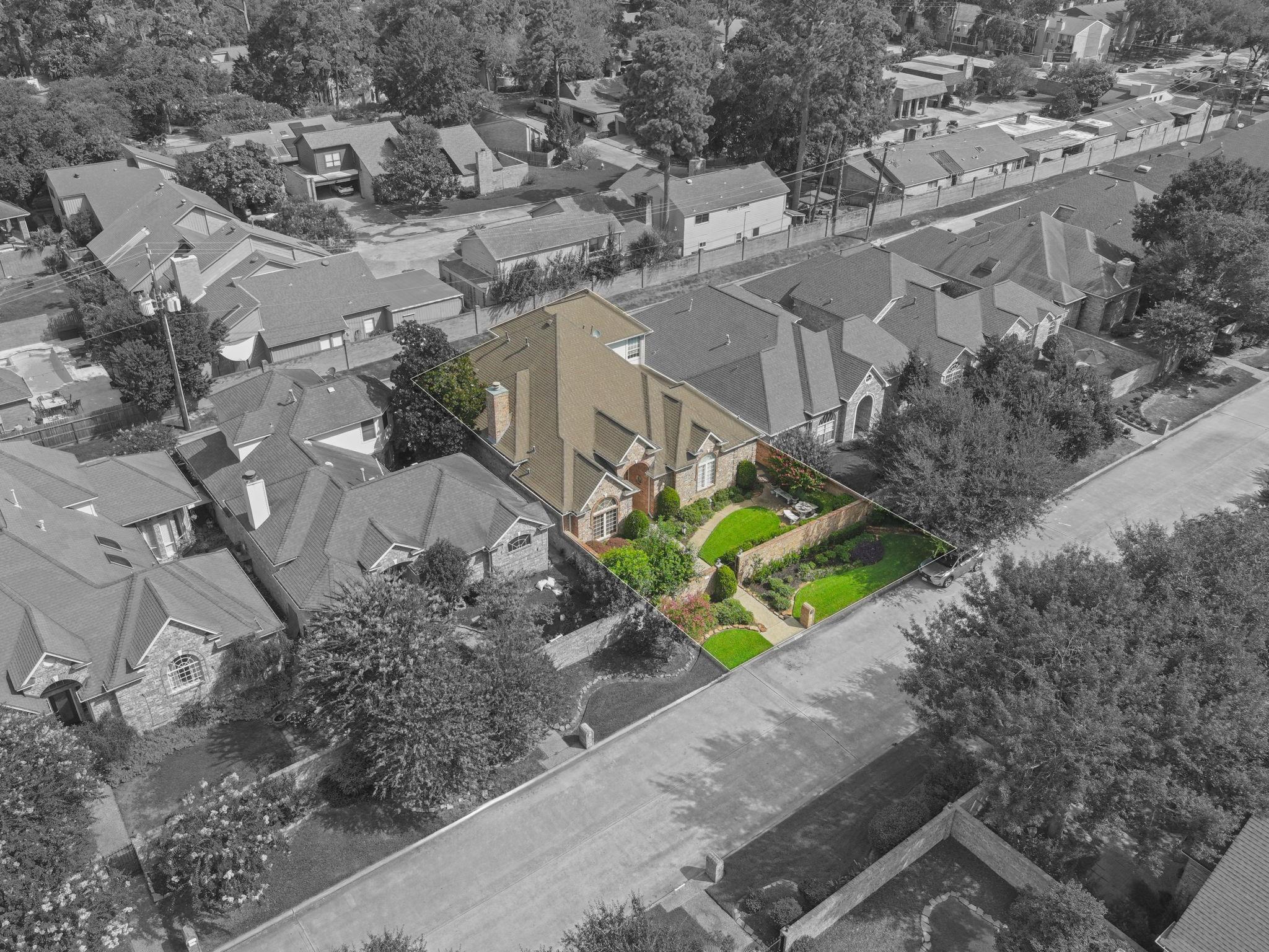 Aerial view of a brick house with a steep roof and landscaped front yard, highlighted among neighboring homes.