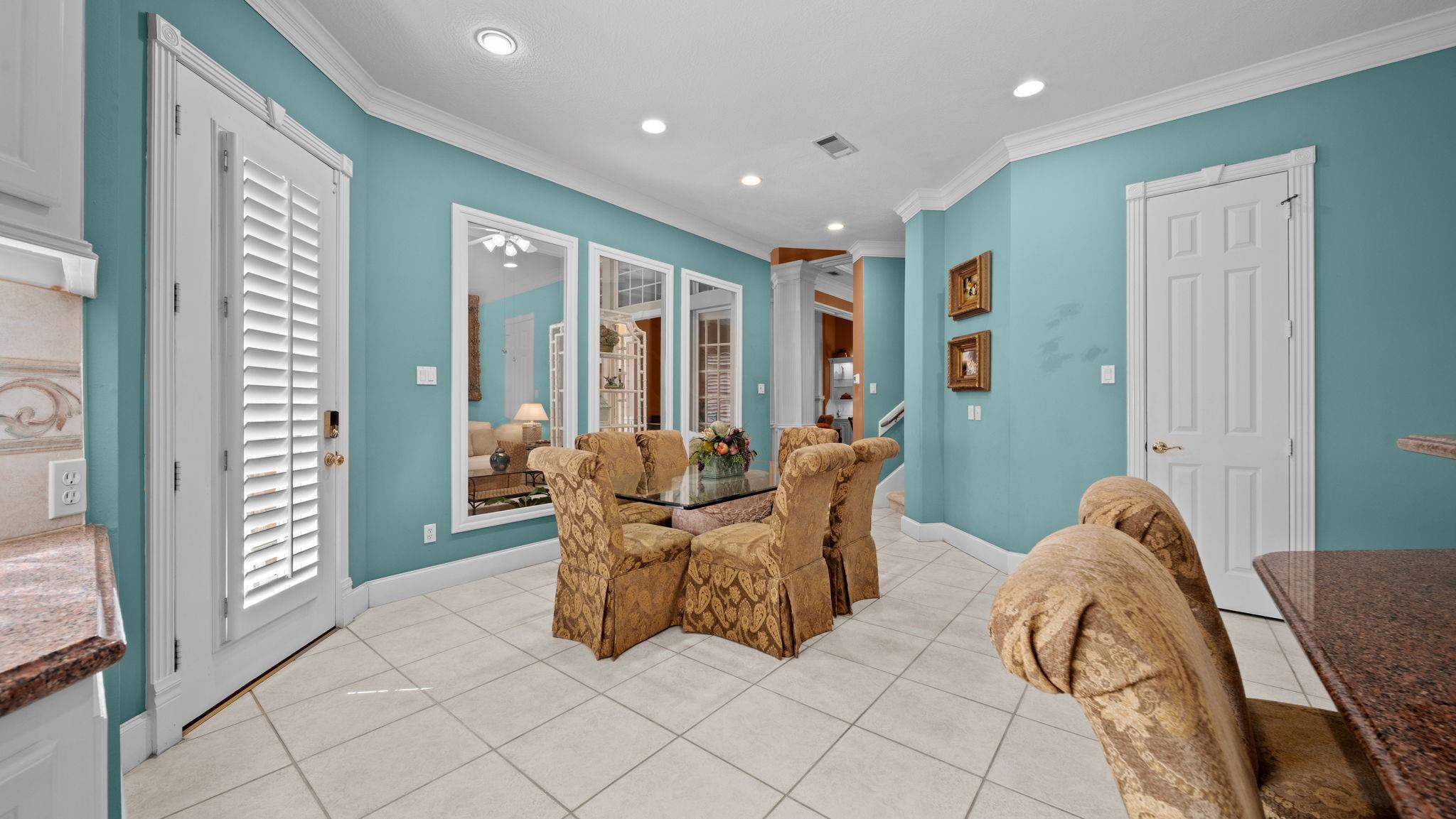 Dining room with a glass-top table, patterned chairs, turquoise walls, and plantation shutters.