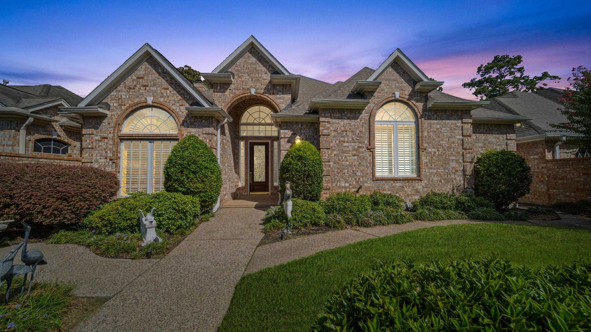 Brick home with multiple gables, arched windows, and a curved garden path at dusk.