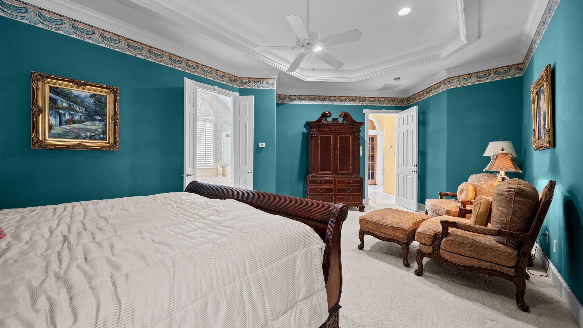 Furnished bedroom with teal walls, a dark wood bed, ornate trim, and upholstered chairs.