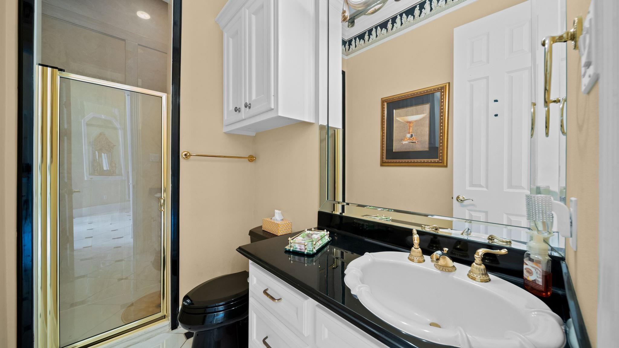 Bathroom with black granite vanity, white sink, gold-tone faucets, and glass-enclosed shower.