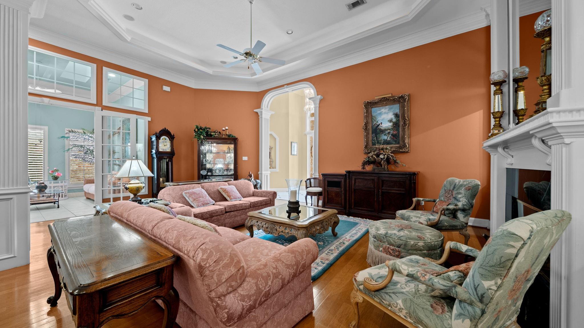 Living room with orange walls, pink sofas, floral armchairs, and a white fireplace.