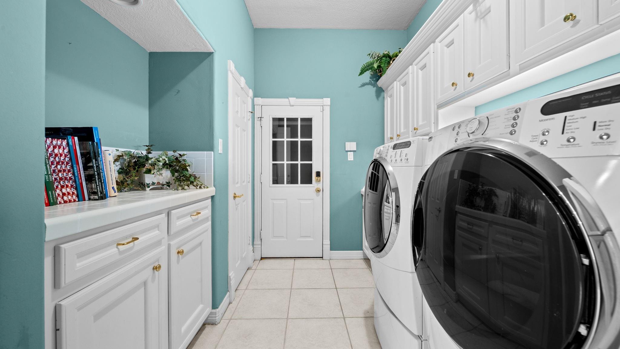 Laundry room with front-loading washer and dryer, white cabinetry, and turquoise walls.