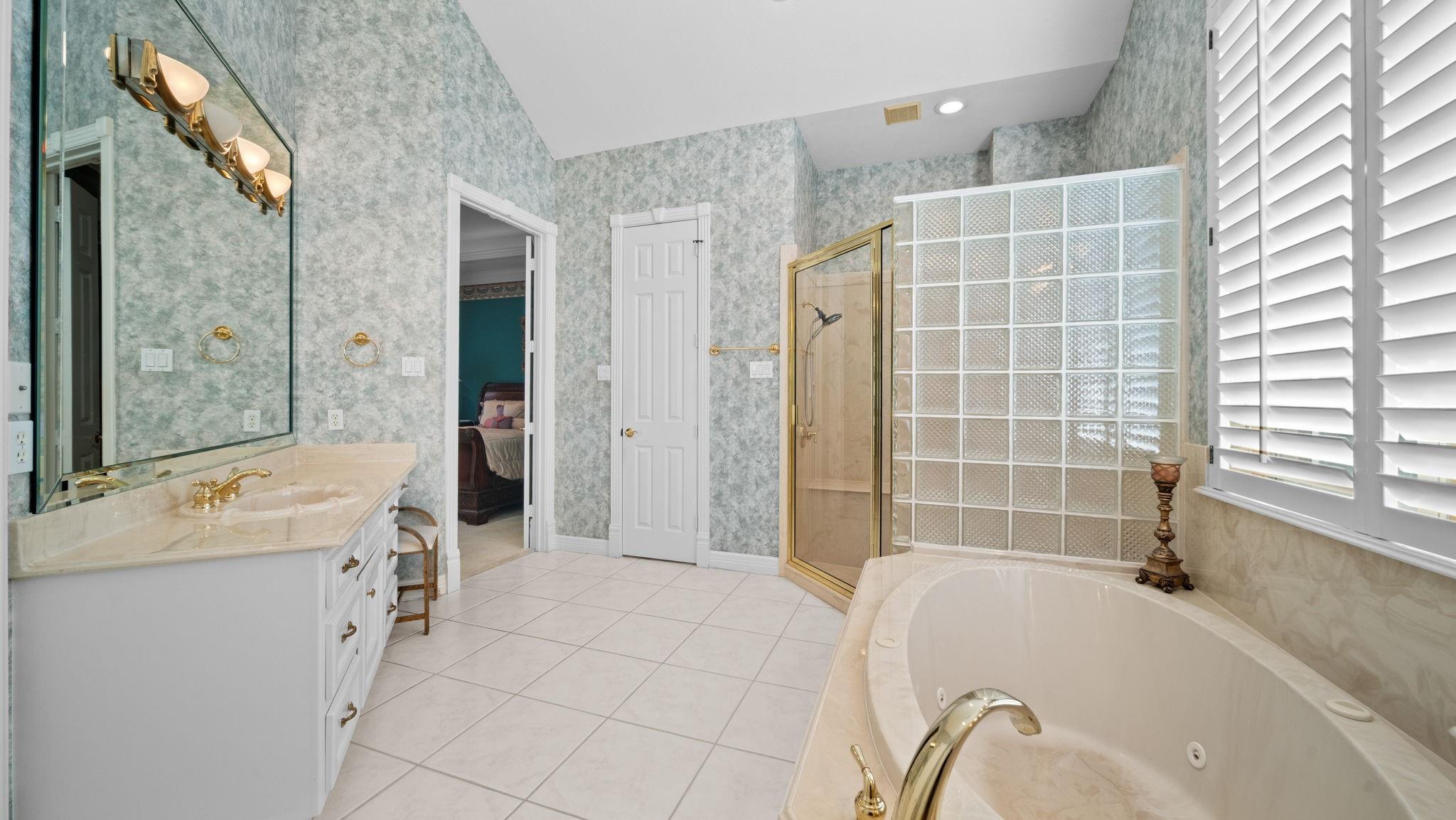 Bathroom with a corner soaking tub, glass-block partition, and cream stone vanity.