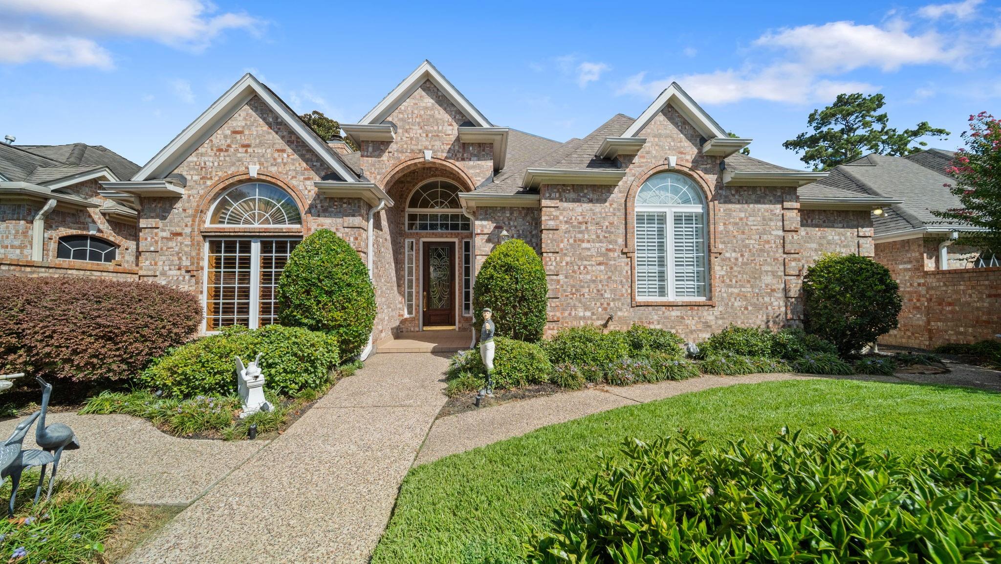 Brick home with peaked gables, arched windows, and a curved walkway through landscaped front gardens.